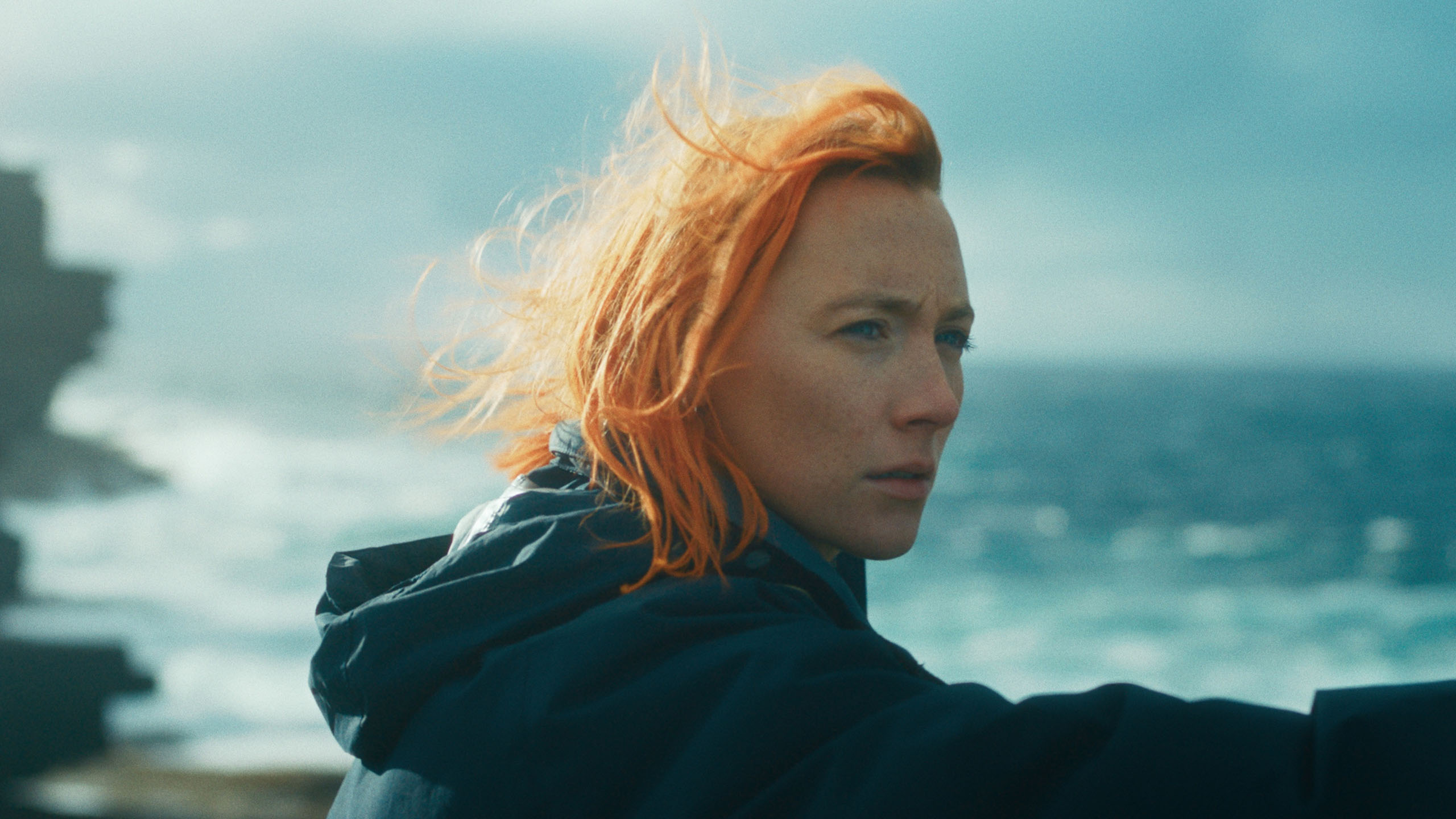 Saorise Ronan's character Rona has bright, orange hair and gazes out across the seaside.
