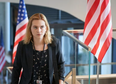 A young woman stands in front of several American flags.