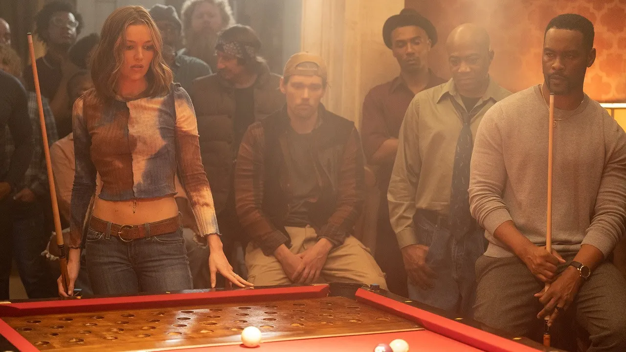 A young woman in a dimly lit room surround by other keno pool players, stands contemplating her next move.