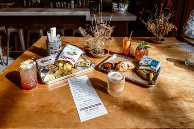 A spread of food, flowers and cocktails on a wooden table.