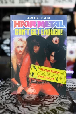 A copy of American Hair Metal: Can't Get Enough sits a top a table covered in stickers. 