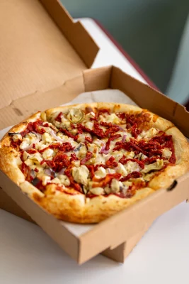 An image of a pizza with a bunch of toppings inside the box. 
