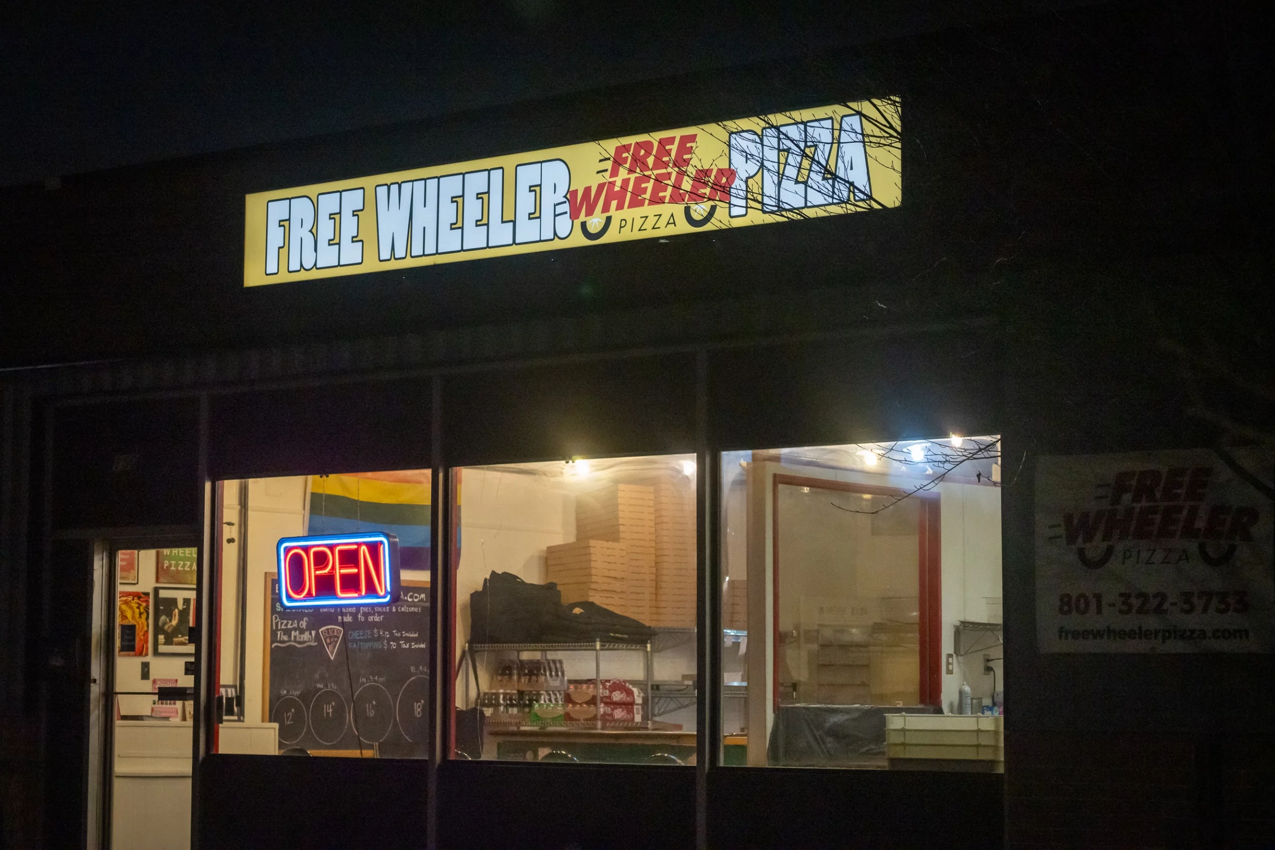 An illuminated sign advertising "Freewheeler Pizza" at night.