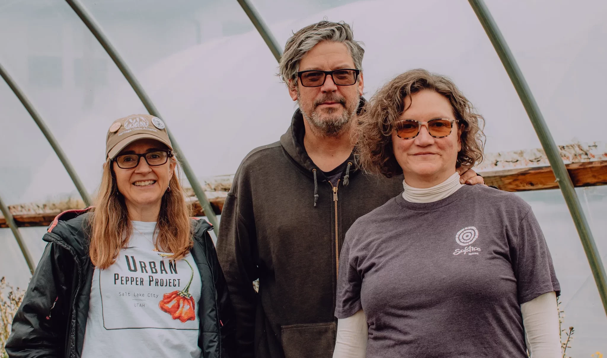 Three people stand inside a greenhouse.