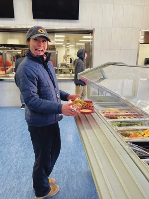 Woman standing across from a food-serving line and smiles.