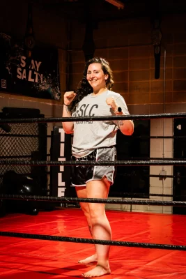 Alexis Whitney smiles in the boxing ring with her fists up.