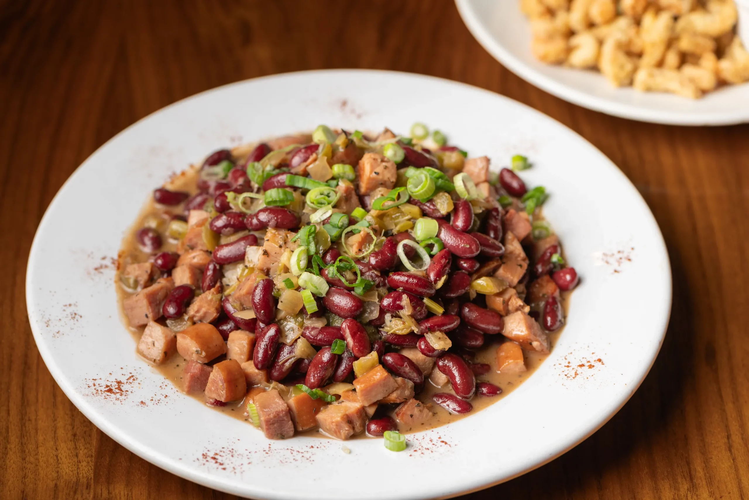 A plate of beans and meat sits on a wooden table.