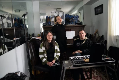 Two members of Flat Rat sit in front on a keyboard, a third member stands behind them in the foreground.