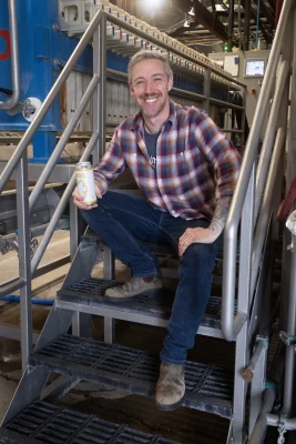 Patrick Bourque sitting on a stairwell inside his distillery with a can of Fonio in his right hand.