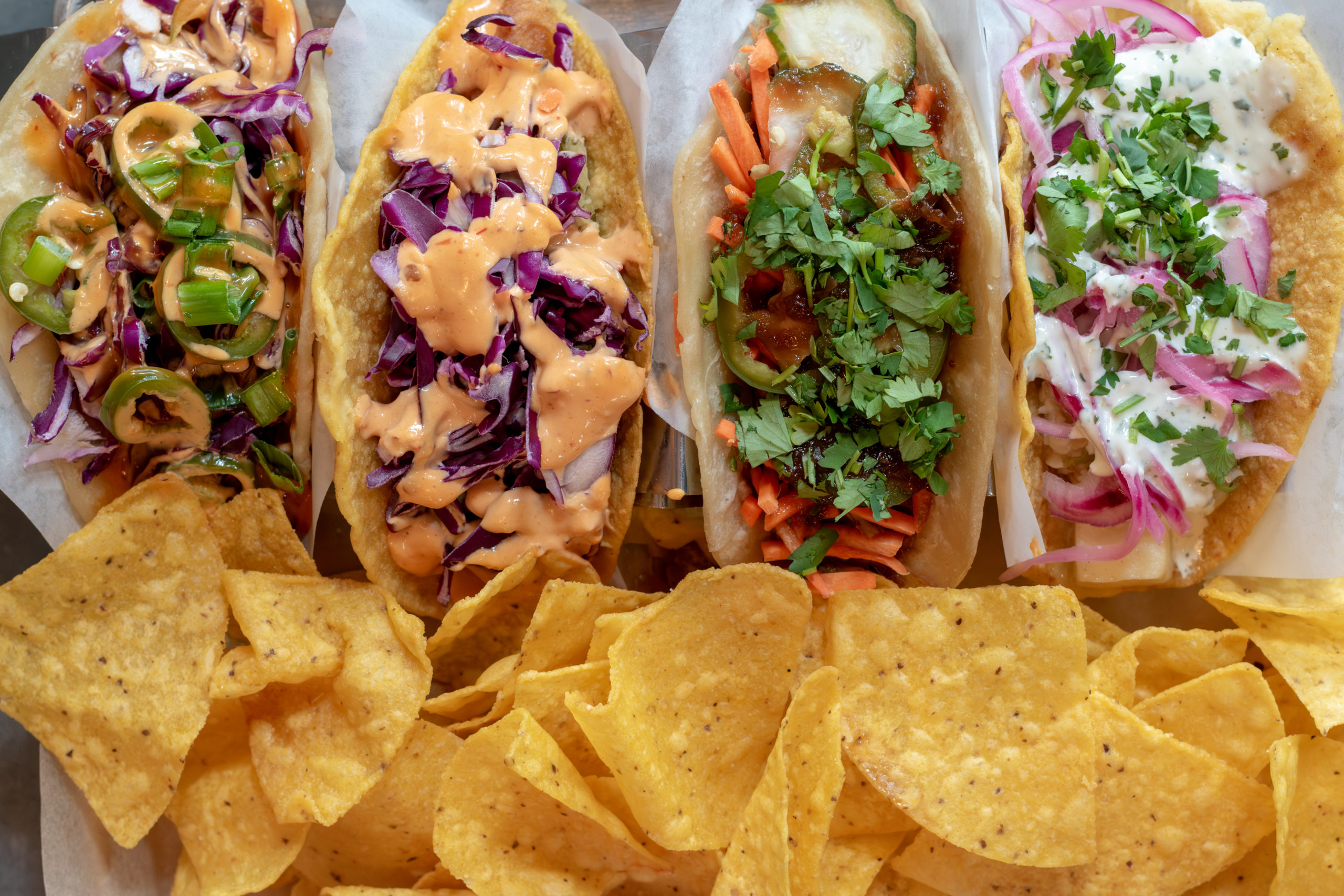 Four tacos on a tray with chips.