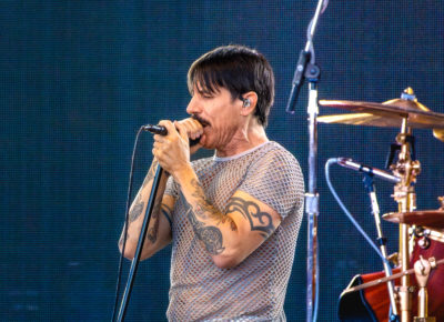 Anthony Kiedis of the Red Hot Chili Peppers sings into the mic, captured at a distance with a few fans at the front of the stage. Photo: @lmsorenson