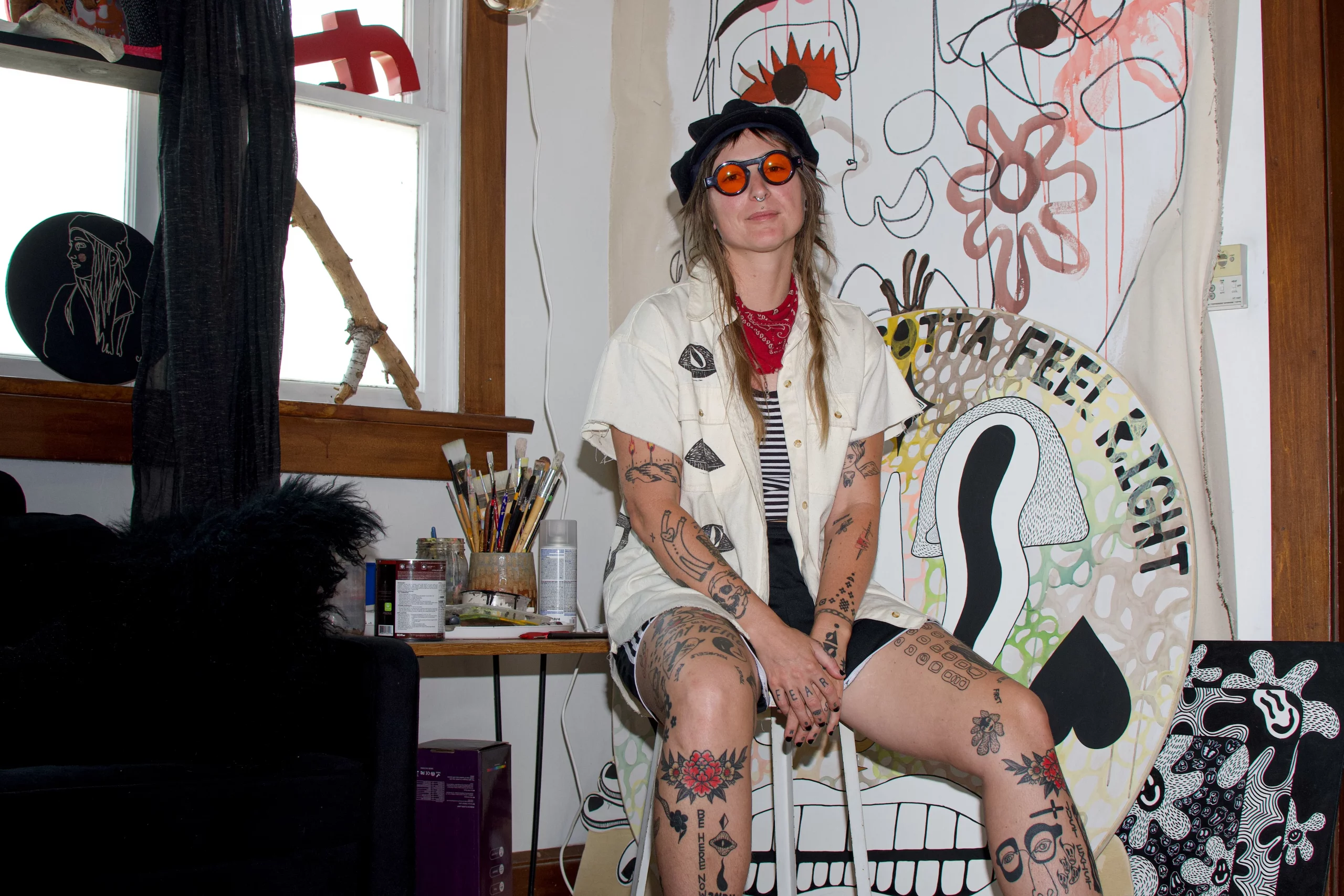 Cake Wish sits in front of an abstract painted wall wearing a white shirt and orange sunglasses.