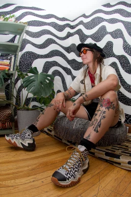Cake sits casually in front of a black and white painted wall wearing chunky sneakers. 