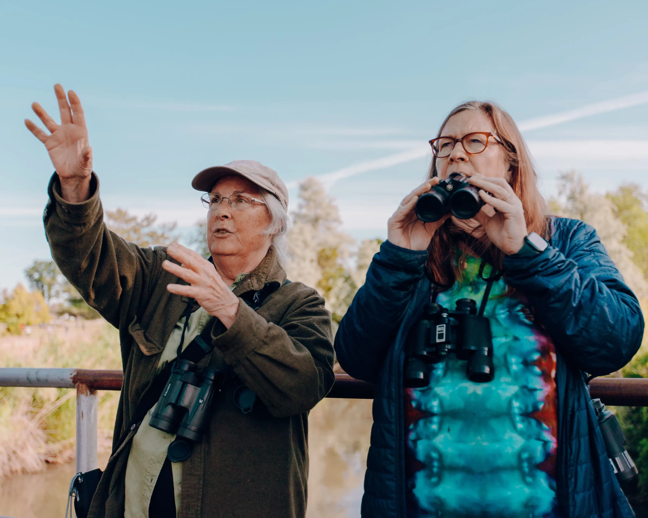Two people standing outside and looking into the distance while holding binoculars.
