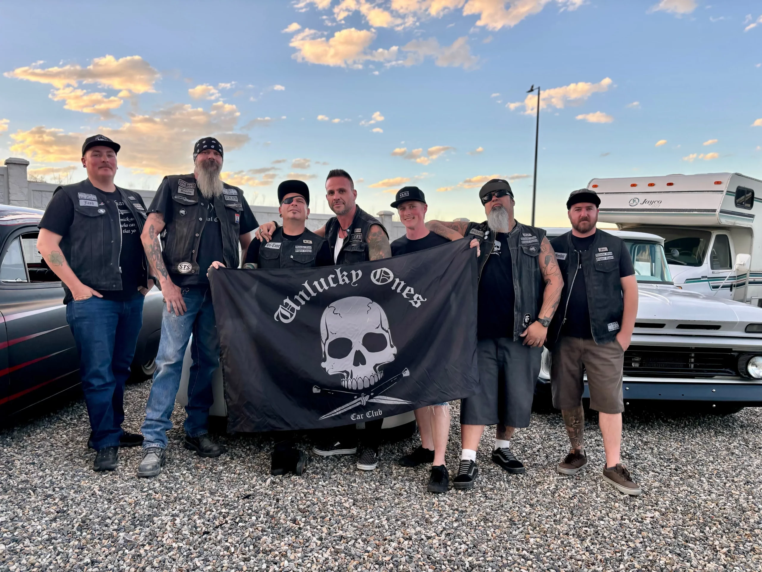 The Unlucky Ones Car Club members stand with their club flag.