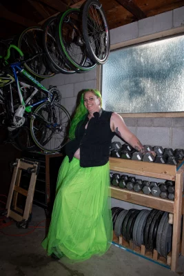 Kelly Green poses with a rack of free weights. Bikes hang from the wall behind her.