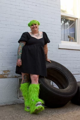 Kelly Green poses against a giant tire wearing bright green, fuzzy platform boots.