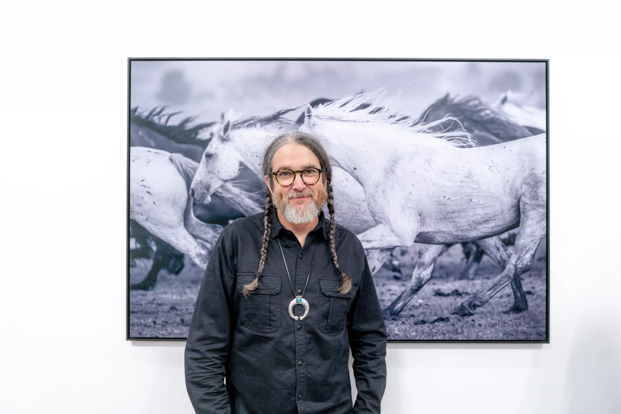 Photography Russel Albert Daniels stands in front of a photograph of horses.