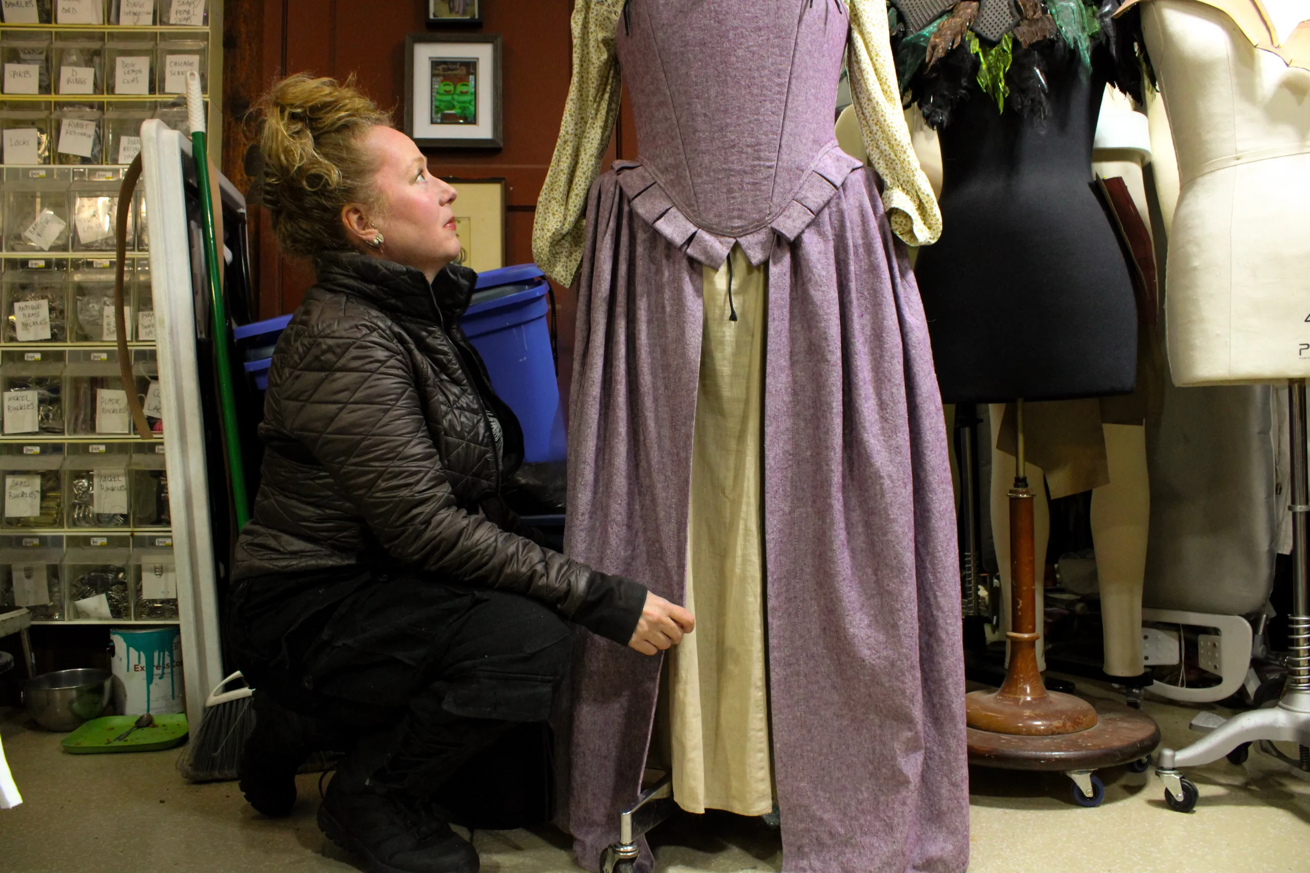 McGrew crouches in front of a cabinet of supplies to adjust a purple and cream dress.