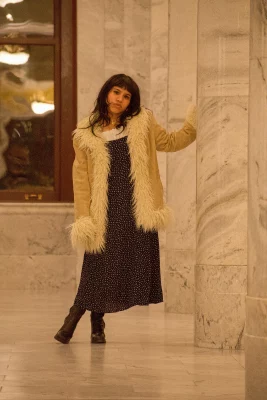 Aura Martinez Sandoval leans against a pillar wearing a fur-lined beige coat.