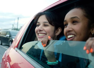 Two girls stick their heads out of the window of a red car.