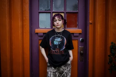 Croft stands in front of a purple and orange door in a Rob Zombie Tee.