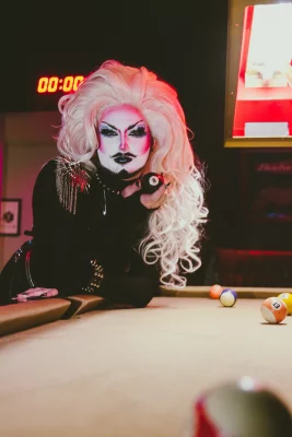 Lorem Ipsum leans over and rests her arms on a pool table with an 8 ball in her hand.