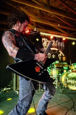 A tattooed man shreds a black guitar on stage at Aces High Saloon.