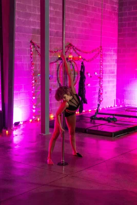 A performer stretches on the pole in a black bodysuit.