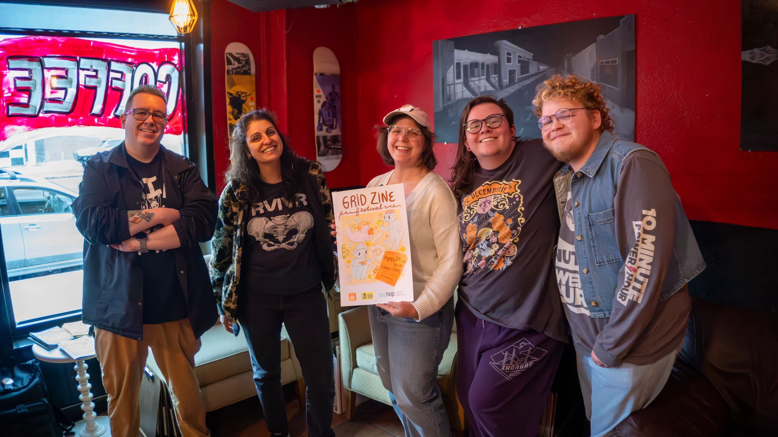 Five people stand shoulder-to-shoulder holding an event poster.