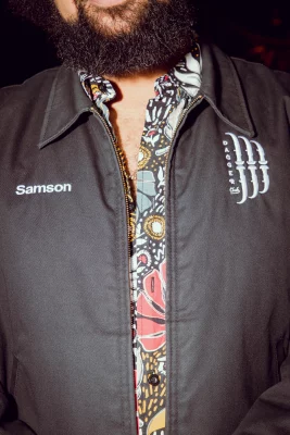 Sam Miller wearing a floral shirt and jacket with his name on it.