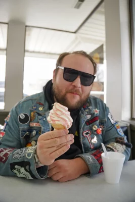A man with sunglasses holds up a cone of soft-serve ice cream.
