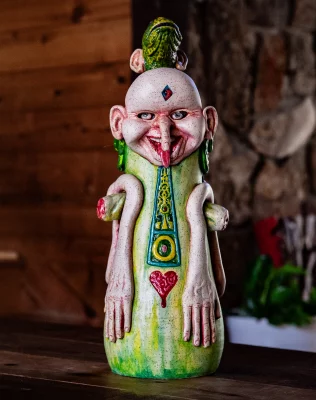 An intricate green jar with a face with a long nose and long flat arms.