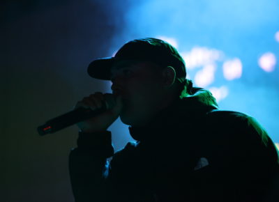 Kneecap’s Mo Chara on stage in SLC at The Depot standing in the shadows with mic to mouth as he stares the audience down. Photo: Logan Sorenson.