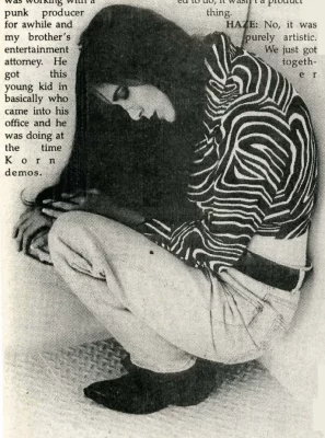 The lead singer of haze crouches in the fetal position on the floor, clad in white jeans and a zebra pattern top. 