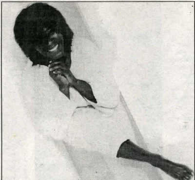 Joan Armatrading sits shoeless in all white clothes.