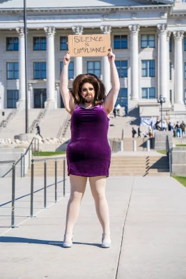 Anya Bacon stands in front of the capitol building holding a protest sign.