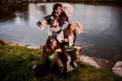 Three actors pose by a river.