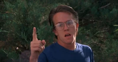 A man in a blue shirt and glasses points as if to express a point.