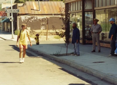 A boy in a yellow shirt walks down a street with people on the sidewalk.